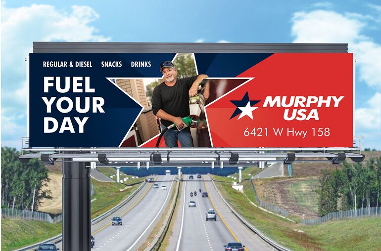 A roadside billboard advertises Murphy USA with the slogan 'Fuel Your Day' on a blue background, a star cutout in the center showing a man pumping gas, and the logo with the address '6421 W Hwy 158' on a red background.