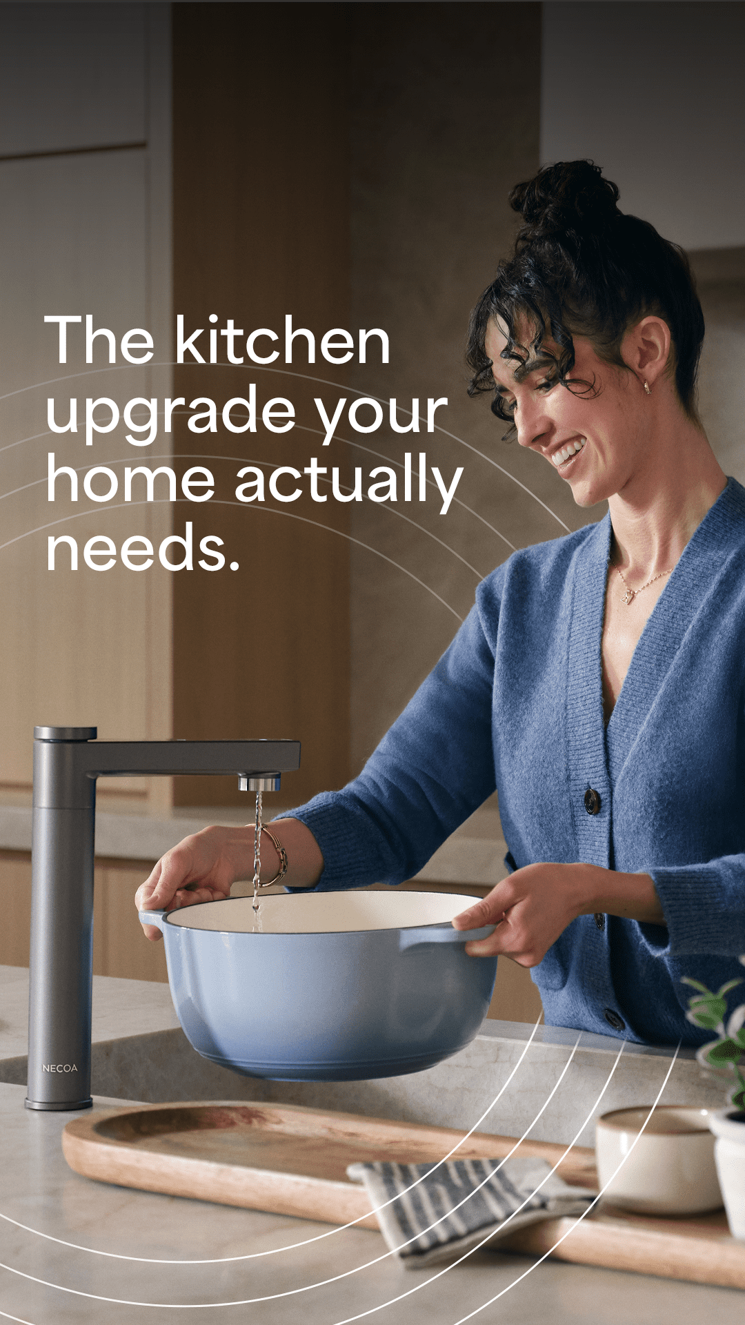 A woman with her hair in a bun smiles as she fills a light blue pot with water from a sleek, dark grey kitchen faucet. Text overlay reads "The kitchen upgrade your home actually needs."