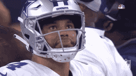 A close-up of Dallas Cowboys quarterback Dak Prescott on the sideline wearing his helmet and looking up with a shocked, wide-eyed expression of disbelief.