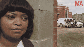 Octavia Spencer as the character Sue Ann ('Ma') peeks around a concrete wall with a suspicious expression, watching a group of teenagers hanging out by a white van in the background.