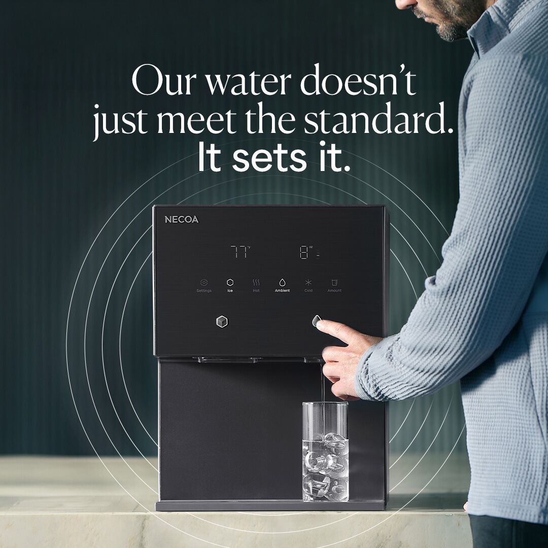 A man in a blue sweater presses a button on a black NECOA water dispenser, filling a glass with ice water. The dispenser has a digital display showing temperature and options for ice, hot, ambient, and cold water.