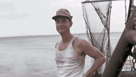A scene from Forrest Gump where Tom Hanks as Forrest Gump stands on his shrimp boat, wearing a white tank top and a cap, smiling and waving enthusiastically.