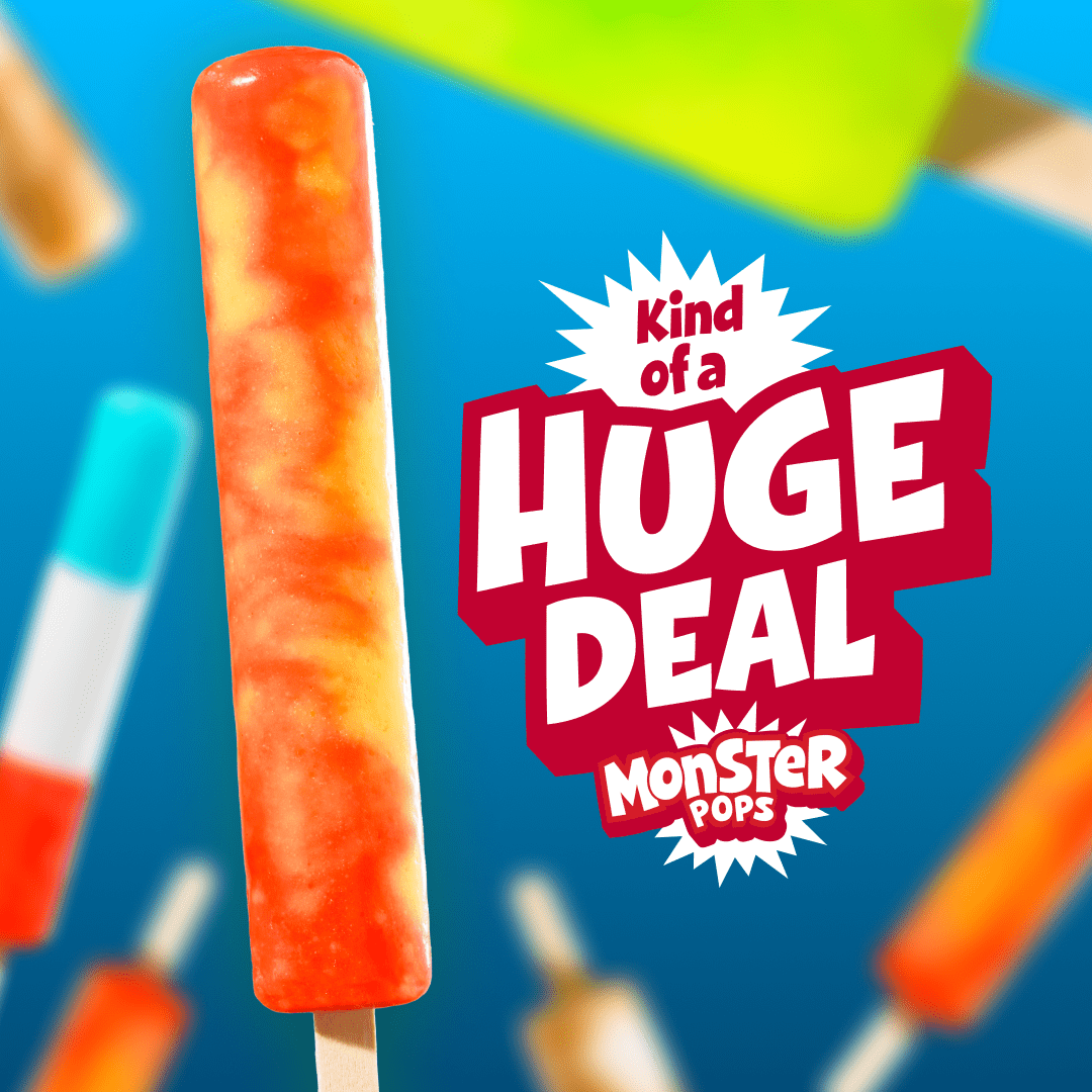A long, vibrant orange and yellow swirled ice pop stands upright against a bright blue background. Next to the popsicle is stylized bold text reading 'Kind of a HUGE DEAL' above the 'MONSTER POPS' logo. Out-of-focus colorful popsicles float in the background.