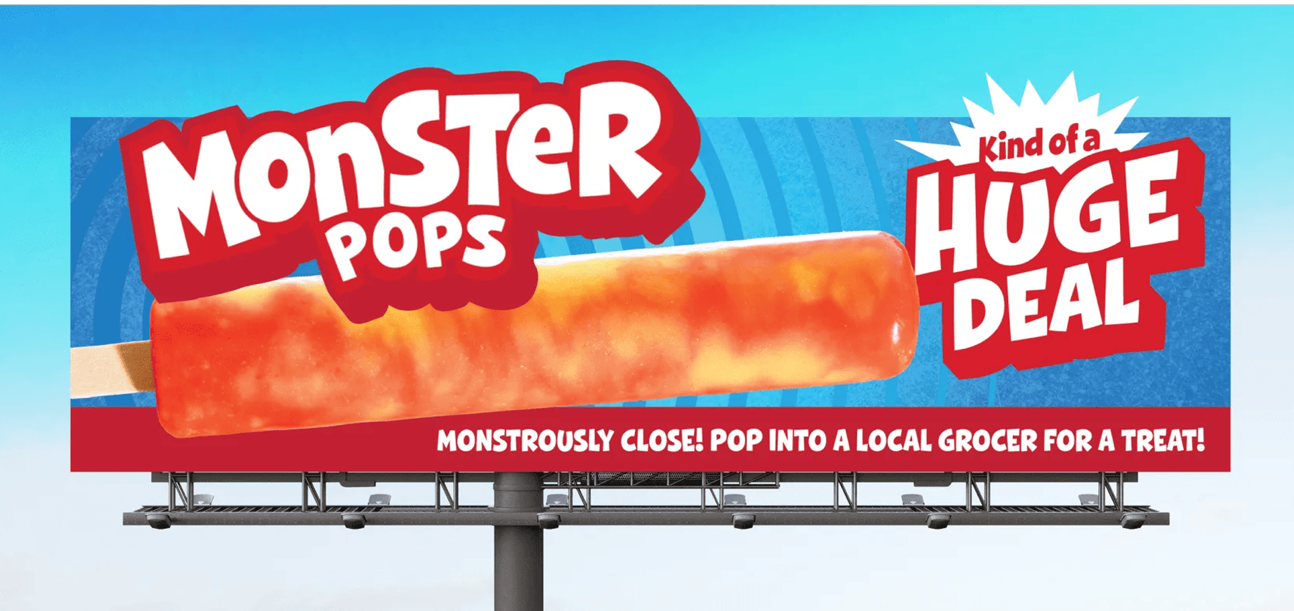 A blue billboard advertising 'Monster Pops' features a large horizontal orange popsicle with text that reads 'MonSTeR POPS', 'Kind of a HUGE DEAL', and a bottom red banner stating 'MONSTROUSLY CLOSE! POP INTO A LOCAL GROCER FOR A TREAT!'.