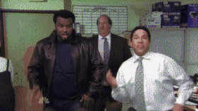 Three men in a sparsely furnished office, two in the foreground are animated and smiling, while the man in the background looks on with a neutral expression.