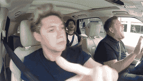 A looping clip from Carpool Karaoke showing Niall Horan pointing directly at the camera from the passenger seat while James Corden laughs hysterically behind the wheel.