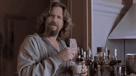 Jeff Bridges as "The Dude" in a grey bathrobe, stirring a White Russian cocktail with a butter knife while looking skeptically towards the camera.