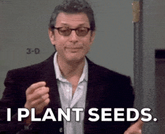 Jeff Goldblum wearing glasses and a dark blazer gestures with his hand under the text overlay 'I PLANT SEEDS.'