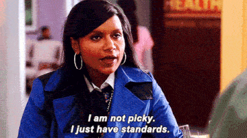 Mindy Kaling as Mindy Lahiri wearing a bright blue coat and large hoop earrings, speaking with the subtitle text: 'I am not picky. I just have standards.'