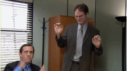 A scene from the TV show 'The Office' showing Dwight Schrute in a grey suit standing up and dancing playfully with his hands raised, while Michael Scott sits in the foreground bobbing his head and clapping.